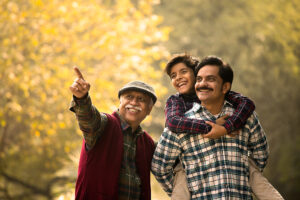 A smiling grandfather, father, and son enjoying a moment together in nature, representing lifelong health and protection.